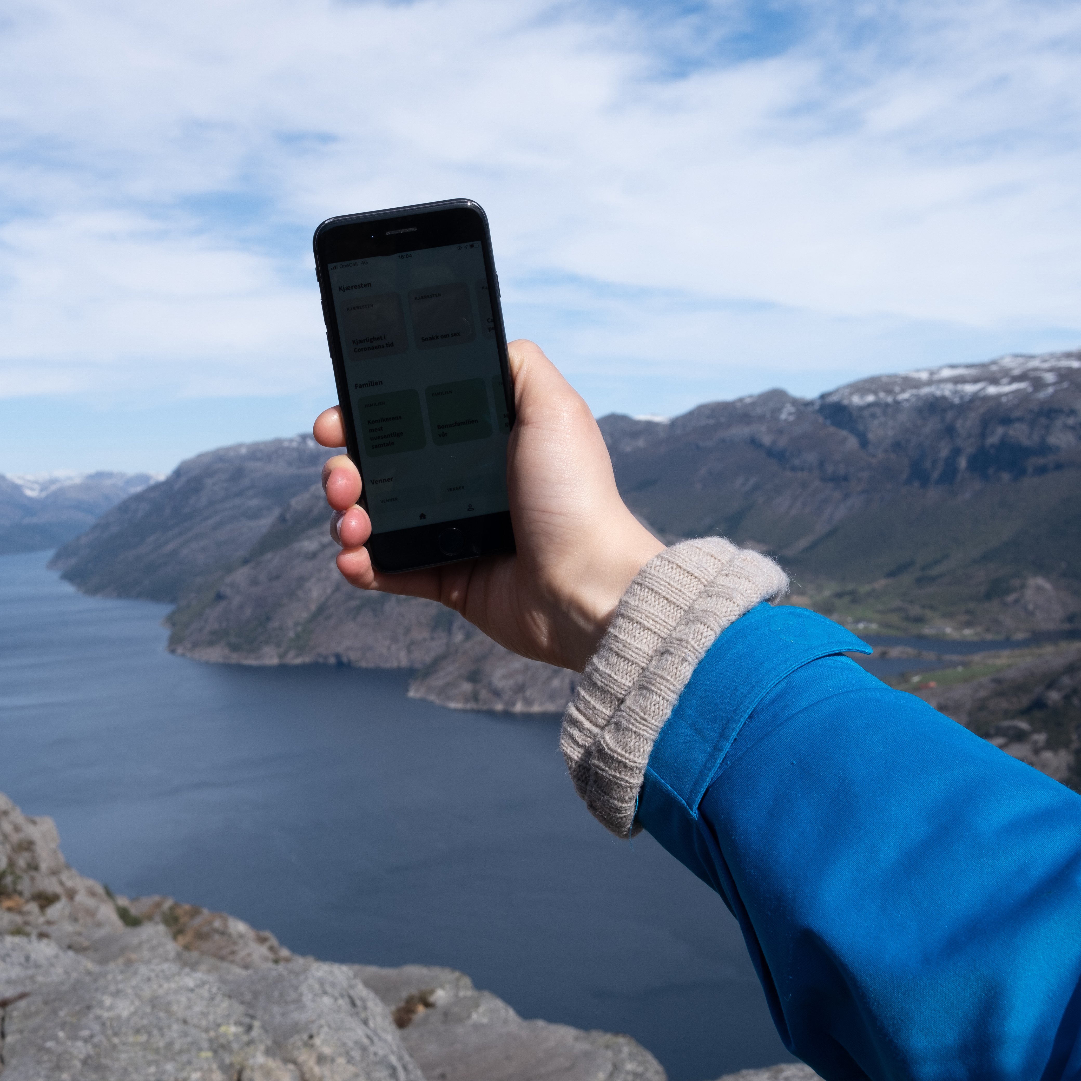 Hånd med mobil med fjord og fjell i bakgrunnen